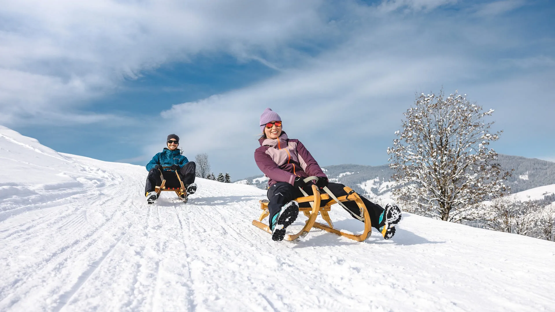 Zwei Personen rodeln auf einer verschneiten Strecke im Brixental, Winterlandschaft.