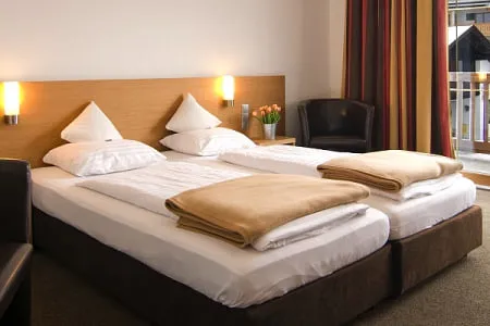 Doppelzimmer mit zwei Betten, Kissen und einem Stuhl, mit Vorhängen im Hintergrund