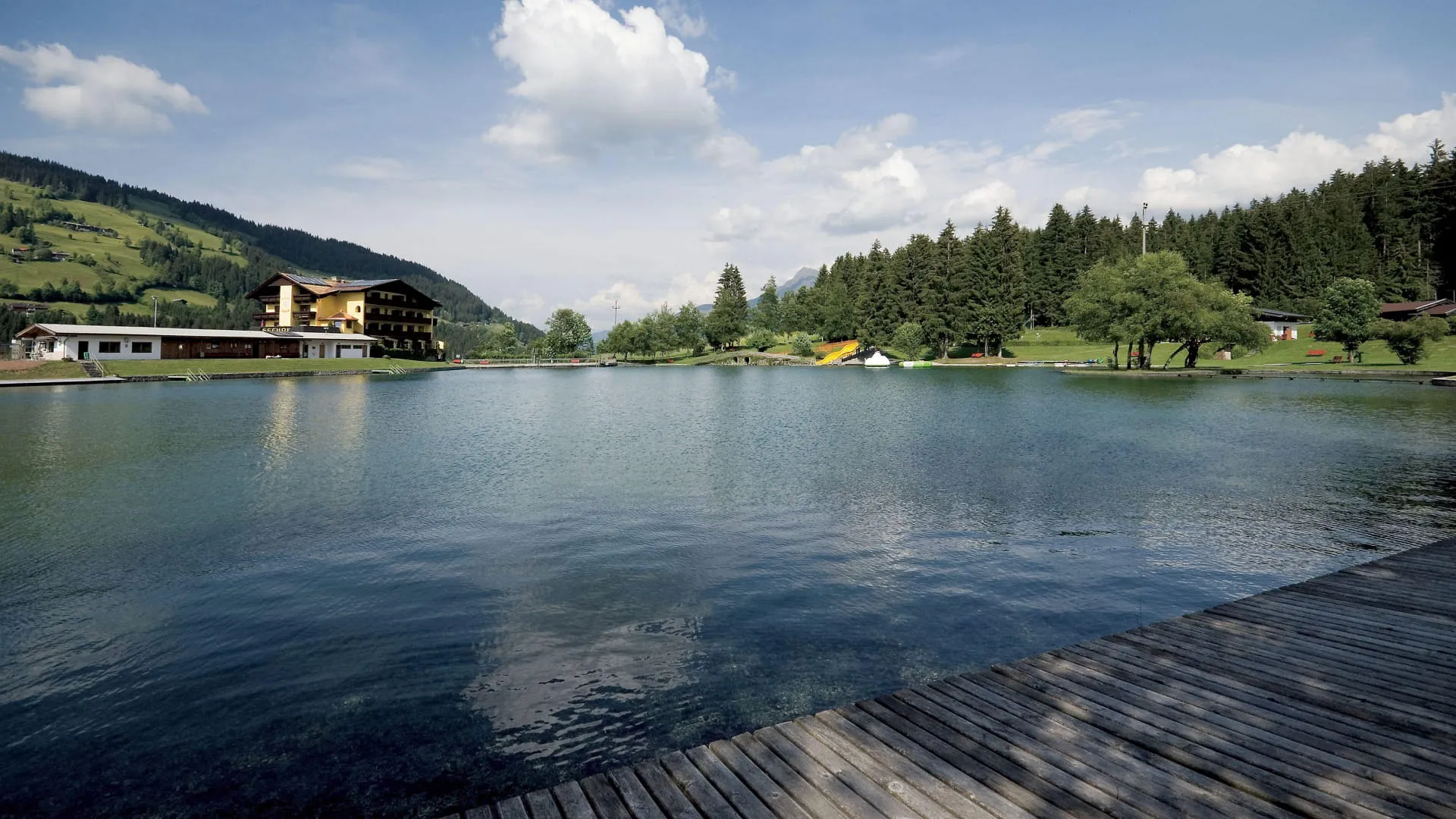 Badesee Kirchberg mit Uferpromenade und Bergen im Hintergrund